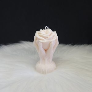Bougie décorative crème en forme de rose entourée de deux mains montantes