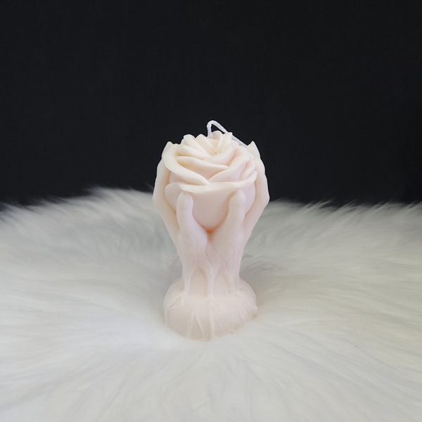 Bougie décorative crème en forme de rose entourée de deux mains montantes