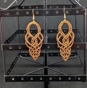 Boucle d'oreilles en macramé marron qui forment des arabesques fluides et harmonieuses.