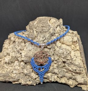 Le pendentif fleur de lotus acier inoxydable argenté et le tour de cou sont réalisés en macramé bleu denim, le tout monté sur une lanière torsadée, dont la longueur est ajustable grâce à son système de nœud coulissant.