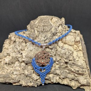 Le pendentif fleur de lotus acier inoxydable argenté et le tour de cou sont réalisés en macramé bleu denim, le tout monté sur une lanière torsadée, dont la longueur est ajustable grâce à son système de nœud coulissant.