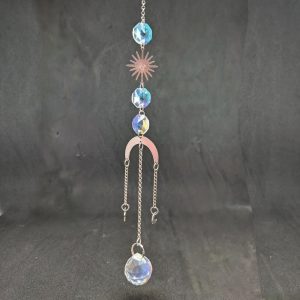 Attrape soleil composé de cristaux de forme octogonale, d'un soleil et d'un arc de lune en métal argenté et fini par 3 chainettes qui se terminent par une petite étoile et une petite lune en métal argenté et au centre par un cristal en forme de boule facettée.